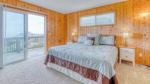 Une chambre avec un grand lit, une porte-fenêtre coulissante donnant sur un balcon et un lambris en bois.