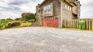 Une maison en bois à deux étages, avec une porte de garage rouge, une allée gravillonnée et une clôture en bois.