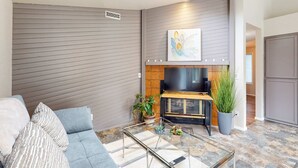 A modern living room with a sofa, a glass coffee table, a fireplace, and a flat-screen TV mounted on the wall. - Well-stocked and centrally located home with patio & enclosed yard (Eugene)