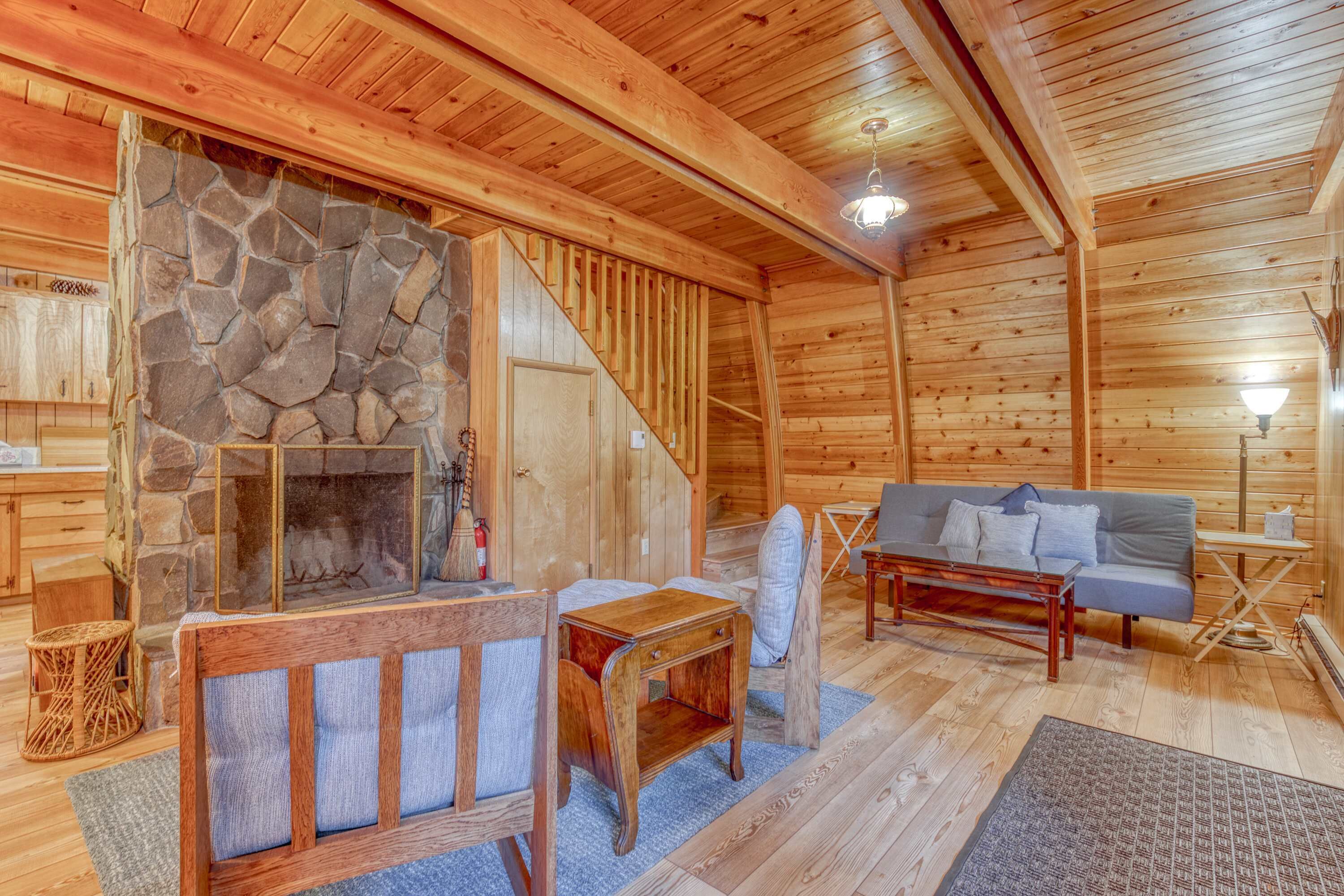Interior de una cabaña de madera con chimenea de piedra, un sofá y una mesa de comedor.