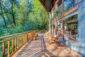Une terrasse en bois avec des fauteuils à bascule donnant sur une zone boisée.
