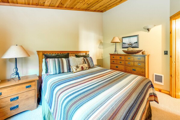 A bedroom with a bed, wooden nightstand, dresser, and a wall-mounted lamp.