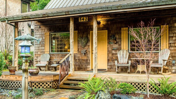 Une maison en bois avec un porche, portant le numéro 542, agrémentée d’un chemin de pierres, d’un espace salon extérieur et d’un petit arbre.