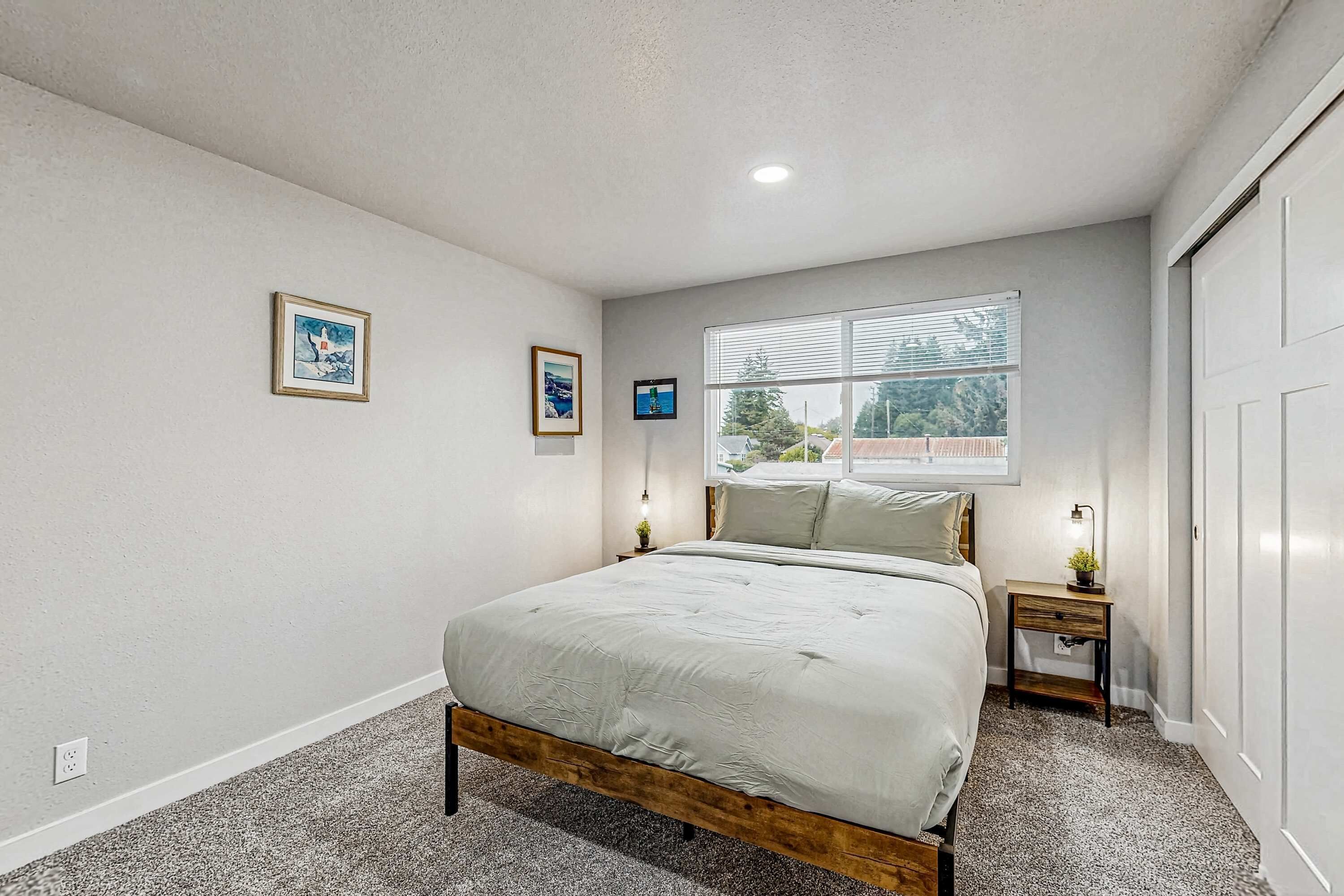 Un dormitorio con cama, ventana, mesita de noche y una lámpara fijada a la pared.