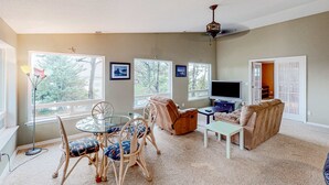 A living room with a glass table, wicker chairs, a sofa, a TV, and large windows.