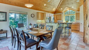 A spacious kitchen with wooden cabinets, a dining area with a large table and chairs, and a view of the outdoors through large windows. - Exquisite home with hot tub, golf on-site, pool, tennis, & washer&dryer (Eagle Crest)