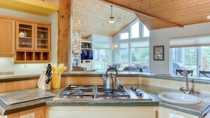 A kitchen with a gas stove, wooden cabinets, and a stone wall. - Exquisite home with hot tub, golf on-site, pool, tennis, & washer&dryer (Eagle Crest)