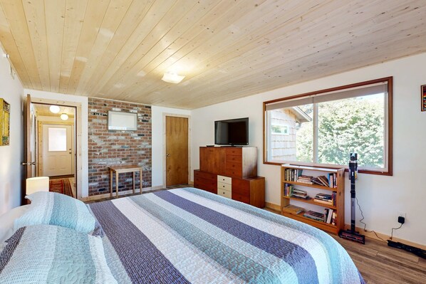 A bedroom with a large bed, a TV, a bookshelf, and a window with a view. - 2-story dog-friendly home with Ping-Pong, gas grill, deck, electric fireplace (Manzanita)