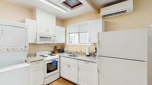 Una cocina con gabinetes blancos, estufa, horno, microondas y refrigerador.