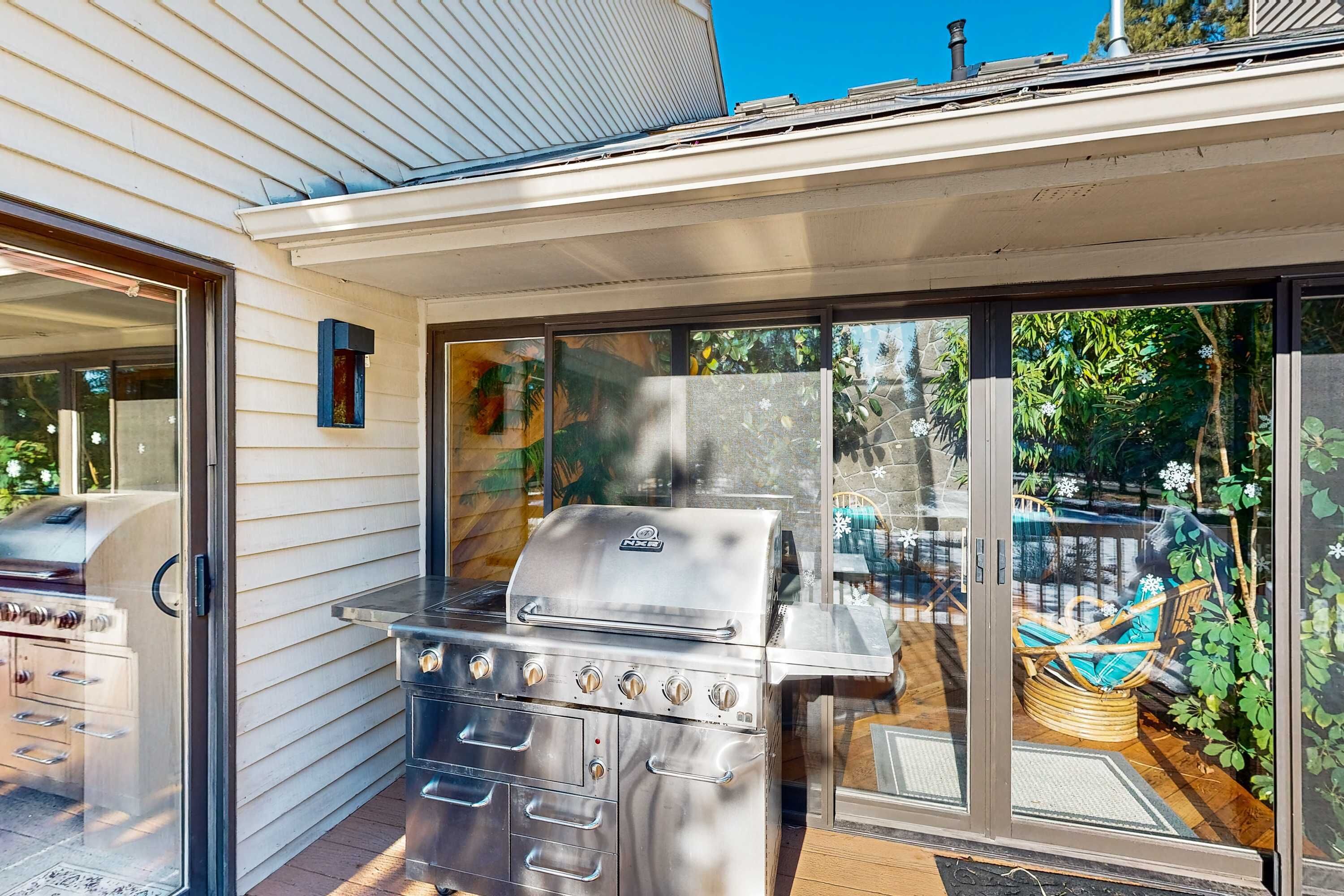 Une terrasse dotée d’un barbecue en acier inoxydable, de portes-fenêtres coulissantes et offrant une vue sur un jardin.