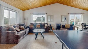 Un'ampia zona giorno con soffitto alto, un divano, un tavolino rotondo e un tavolo da ping pong.