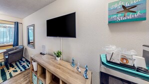 A hotel room with a flat-screen TV, a wooden desk, a chair, a small plant, decorative starfish, and a trash bin. - Retro beach experience with fast WiFI - walk to downtown shops & eateries (Bandon)