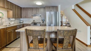 Eine Küche mit Holzschränken, einem Edelstahlkühlschrank, Granitwerkplatten und einem Essbereich mit Holzbänken.