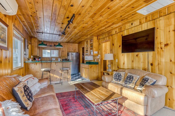 A wooden cabin interior with a living room, kitchen, and bar area.