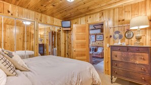 A wooden-paneled room with a bed, dresser, television, and a door leading to another room. - Cozy pine interior home in the heart of Government Camp (Government Camp)