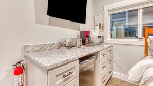 A modern kitchen with a marble countertop, a built-in oven, a coffee maker, and a fire extinguisher.