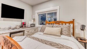 A bedroom with a bed, bedside table, desk, and a window.