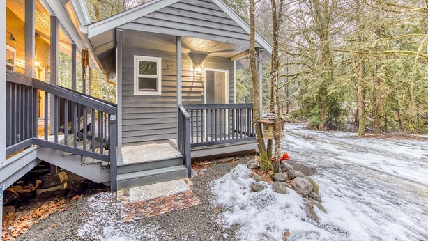 A house with a porch, a staircase leading to the entrance, and a view of the surrounding forest.