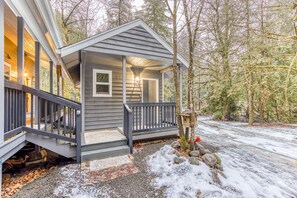 A house with a porch, a staircase leading to the entrance, and a view of the surrounding forest. - Inviting studio with kitchenette & scenic forest setting (Welches)