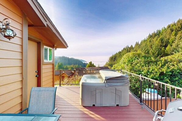 Une terrasse dotée d’un jacuzzi, de chaises et offrant une vue sur une colline boisée.