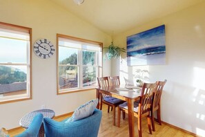 Un coin repas avec une table et des chaises en bois, une horloge et un tableau représentant un paysage marin.