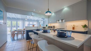 A modern kitchen with a central island, bar stools, and a dining area with a view. - Modern villa in Safir (Noord) with private pool and outdoor kitchen. Minutes from Eagle & Palm Beach. Perfect for relaxing, dining outside, and enjoying Aruba’s best beaches in comfort and style. (Noord)