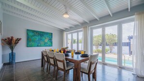 A dining area with a large table, chairs, and a view of a swimming pool. - Modern villa in Safir (Noord) with private pool and outdoor kitchen. Minutes from Eagle & Palm Beach. Perfect for relaxing, dining outside, and enjoying Aruba’s best beaches in comfort and style. (Noord)