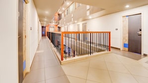 A hotel corridor with a tiled floor, a wooden railing, and a door with a blue accent.