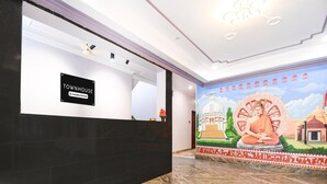 A reception area with a black reception desk, a mural depicting a temple and a seated figure, and a tiled floor.