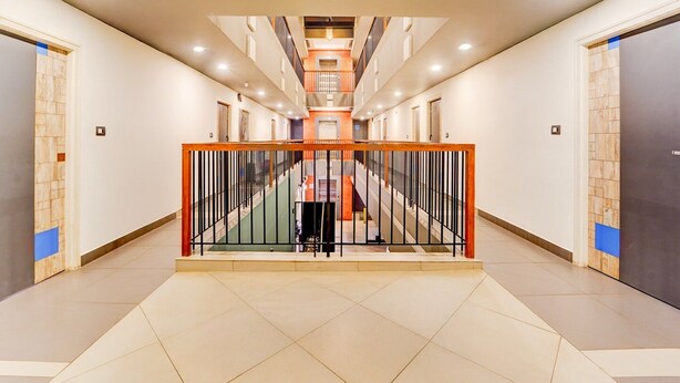 A modern hotel lobby with a central staircase, multiple doors, and a tiled floor.