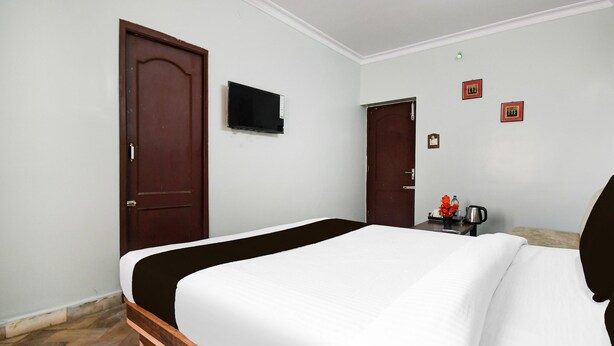 Habitación de hotel con cama, televisión, puerta y una pequeña mesa con tetera y flores.