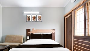 A hotel room with a bed, a chair, a nightstand, and a window with blinds.