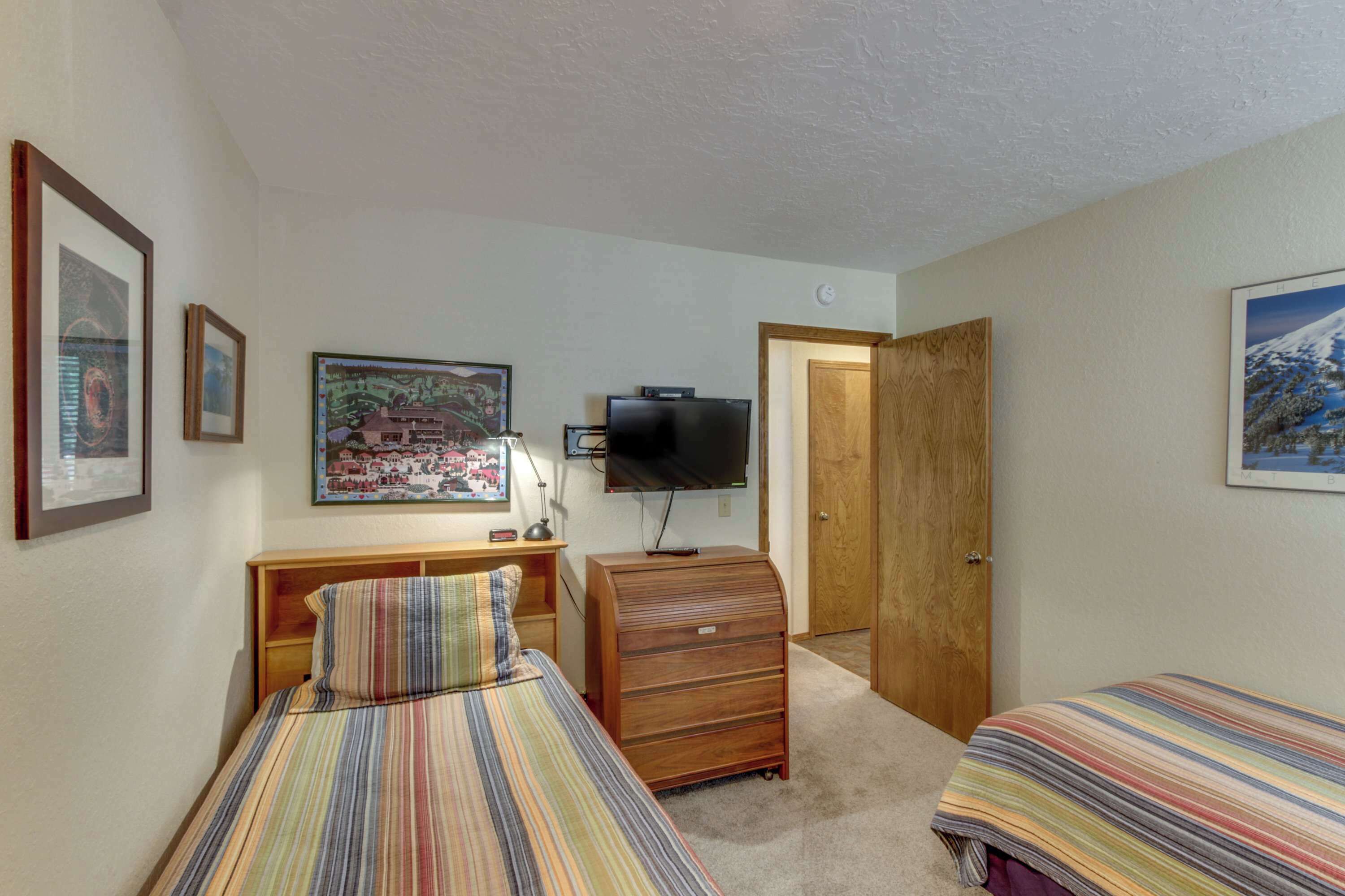 A bedroom with two beds, a television, a dresser, and framed pictures on the walls.