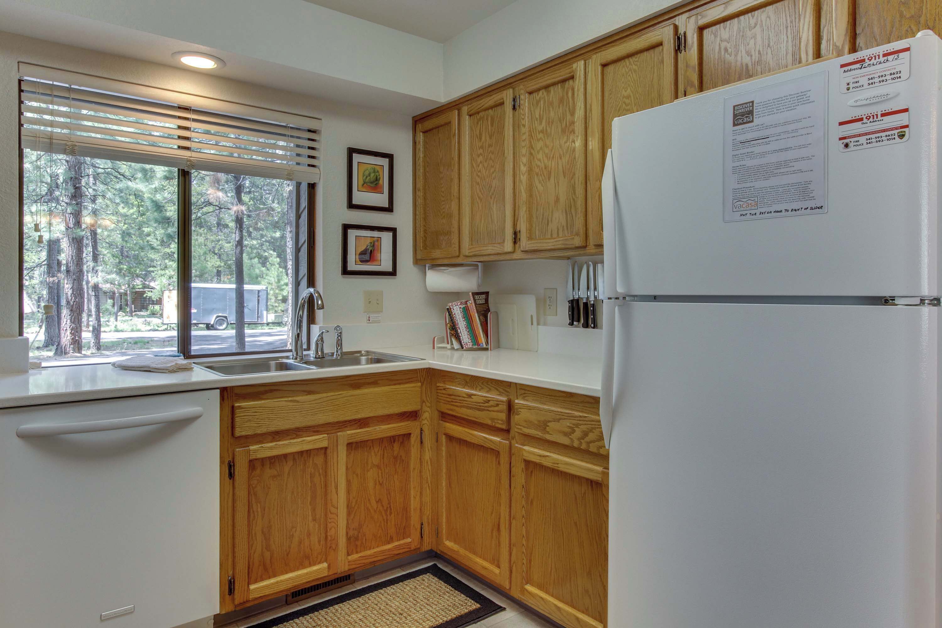 A kitchen with wooden cabinets, a white refrigerator, a window with blinds, and a sink.
