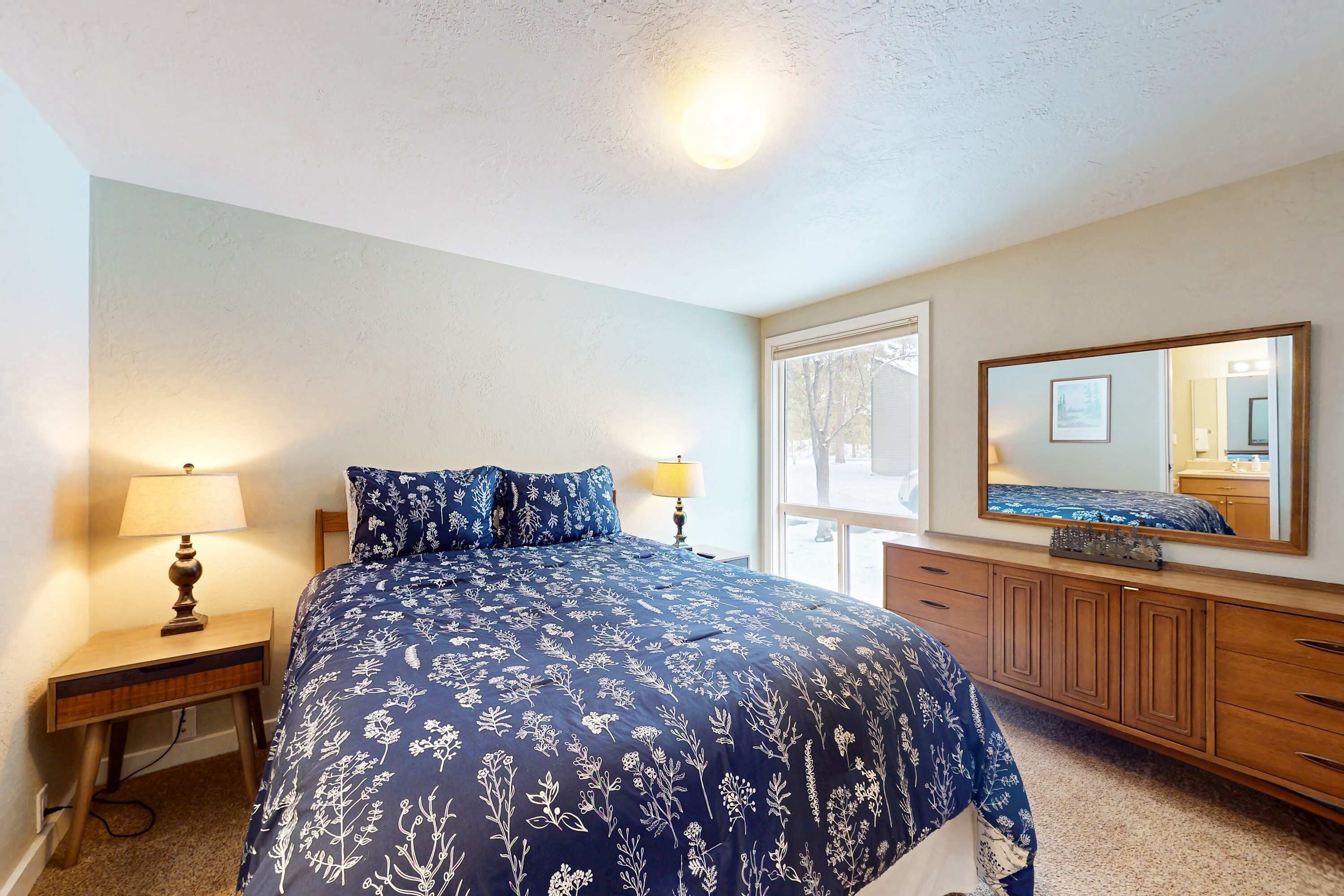 A bedroom with a bed, a nightstand, a dresser, a mirror, and a window.