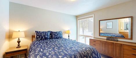 A bedroom with a bed, a nightstand, a dresser, a mirror, and a window.