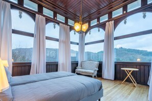 A bedroom with a bed, a chair, a small table, and large windows with curtains. - Elegant Castle for 19 Guests (La Roche-en-Ardenne)