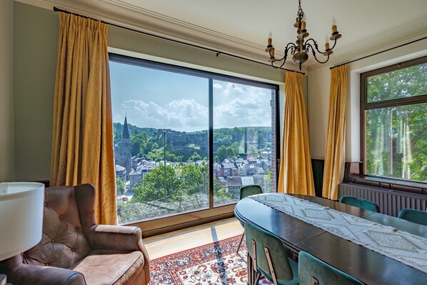 A room with a large window, a dining table, a chandelier, and a view of a cityscape. - Elegant Castle for 19 Guests (La Roche-en-Ardenne)