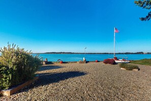 Ein Kiesstrand mit Segelboot und amerikanischer Flagge, ein klarer, blauer Himmel und ferne Hügel.