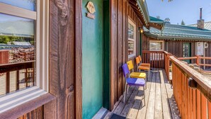 A wooden deck with a green door, a welcome sign, and a view of a building with a chimney. - Mountain & valley-view dog-friendly cabin with courtyard, partial AC, and WiFi (White Salmon)
