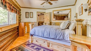 A log cabin-style bedroom with a bed, wooden headboard, a ceiling fan, and a large mirror. - Mountain & valley-view dog-friendly cabin with courtyard, partial AC, and WiFi (White Salmon)