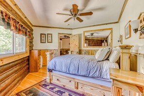 A log cabin-style bedroom with a bed, wooden headboard, a ceiling fan, and a large mirror.