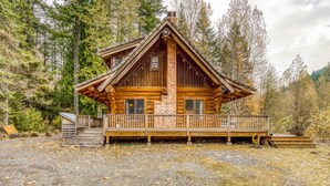 Een vakantiehuis in blokhutstijl met een houten terras, schoorsteen en veranda.