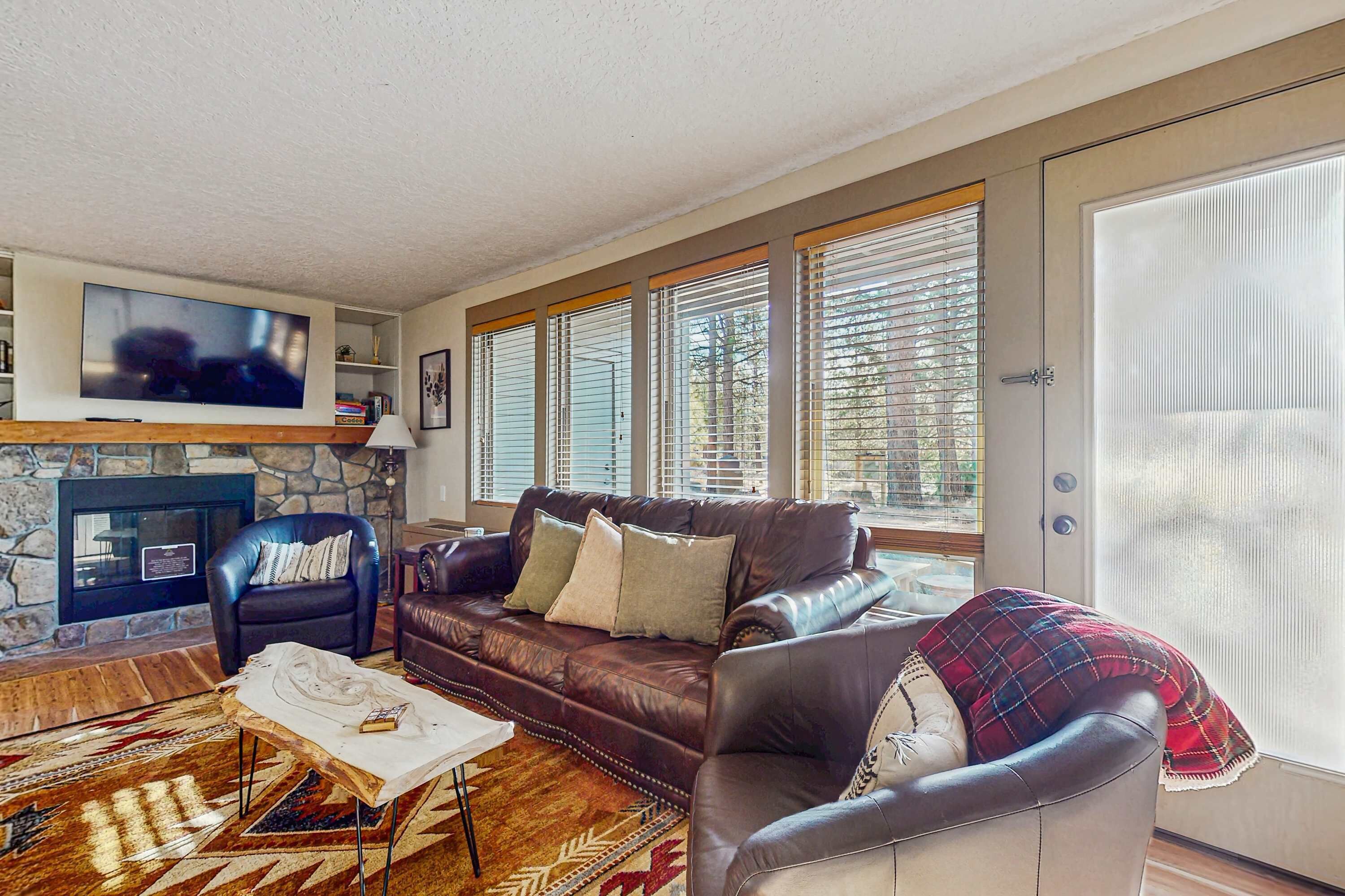 A living room with a stone fireplace, leather sofa, and a television mounted on the wall.