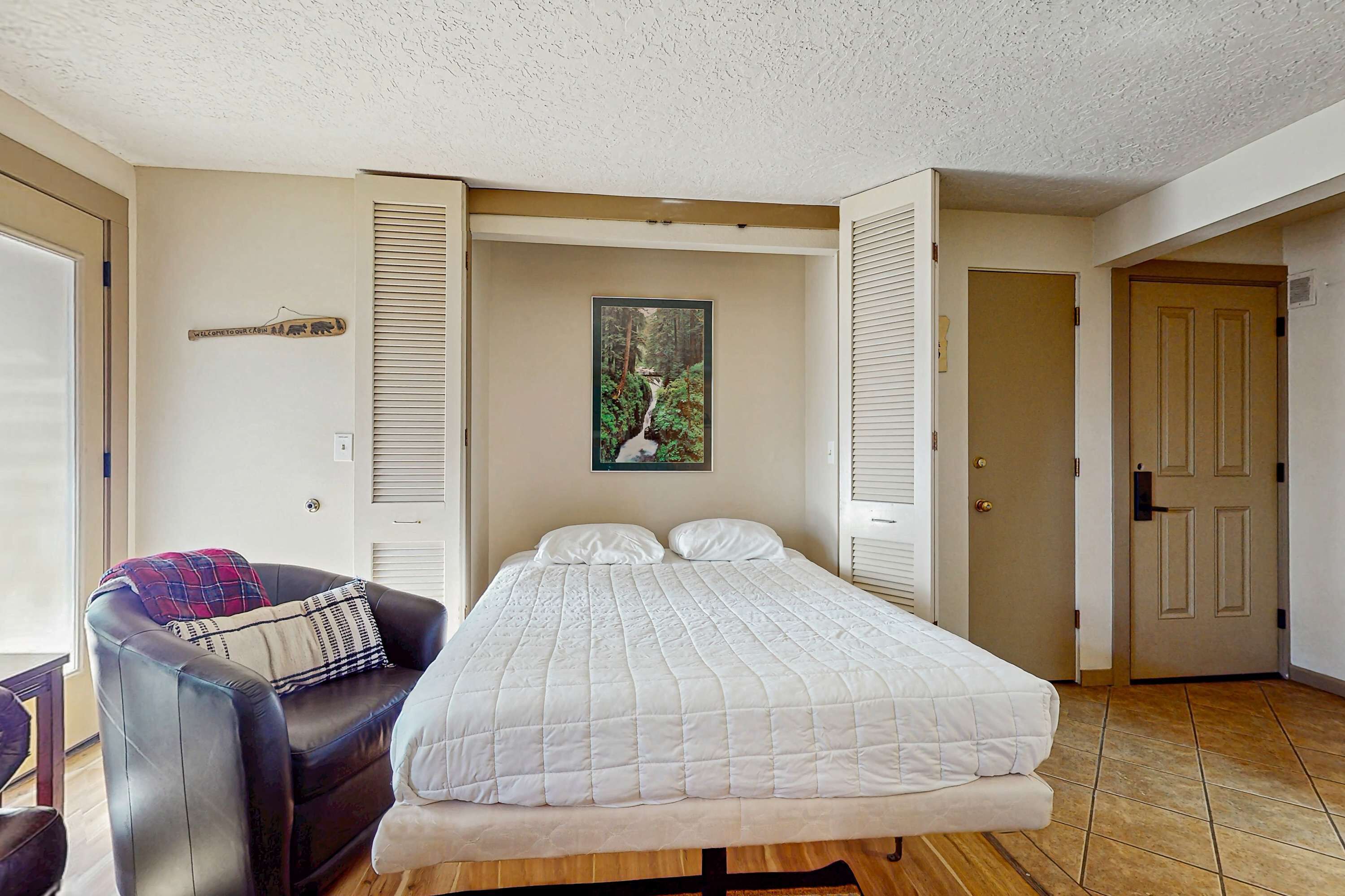 A bedroom with a bed, a sofa, a door, and a wall-mounted picture.