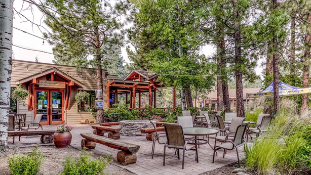 An outdoor patio with wooden furniture, a stone pathway, and a building with a wooden facade. - Dog-friendly ground-floor condo with pools, hot tubs, sauna, & fitness room (Bend)