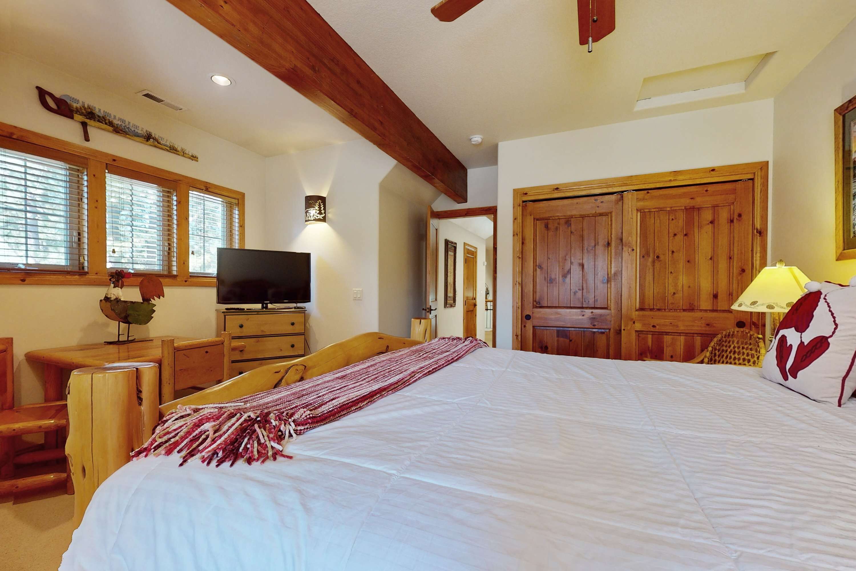 A bedroom with a large bed, wooden furniture, a television, and a window with blinds.