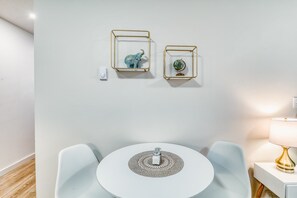 Una habitación minimalista con una mesa redonda, dos sillas, una lámpara de pared y dos obras de arte enmarcadas.