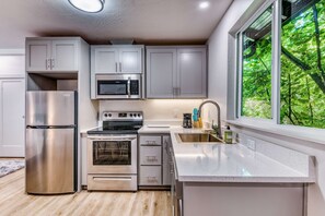 A modern kitchen with stainless steel appliances, white cabinetry, and a window with a view of greenery. - Downtown studio - walk to University - full kitchen, dog-friendly, washer/dryer (Eugene)