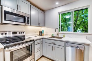 Una cocina moderna con electrodomésticos de acero inoxidable, armarios grises, lavavajillas y ventana con vistas a zonas verdes.